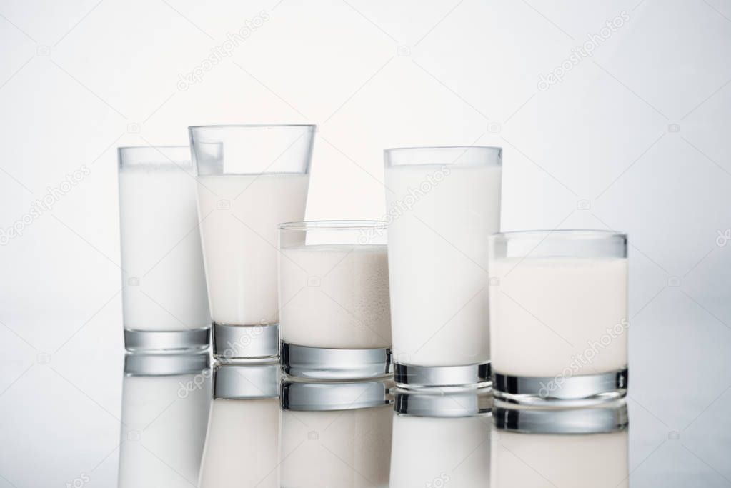 row of glasses with fresh alternative milk on grey background with reflection