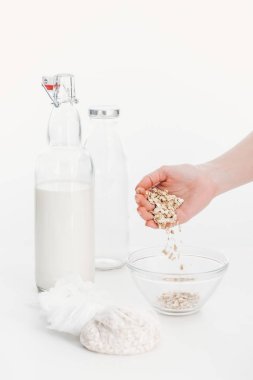 cropped view of woman putting oat flakes in bowl while cooking oat vegan milk clipart