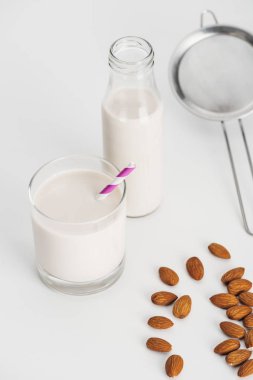organic almond milk in bottle and glass with straw near scattered almonds and sieve clipart