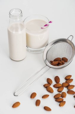 vegan almond milk in bottle and glass with straw near scattered almonds and sieve clipart