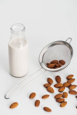 vegan almond milk in bottle near scattered almonds and sieve on grey background clipart