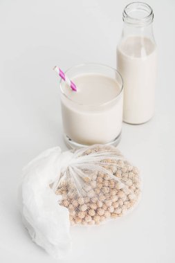 chickpea in white cheesecloth near bottle and glass with vegan chickpea milk on grey background clipart