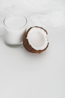 organic vegan coconut milk in glass near coconut half and cheesecloth on grey background clipart