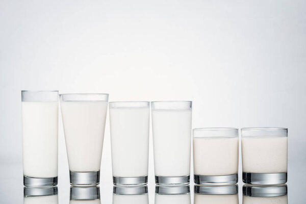 row of glasses with organic vegan milk on grey background