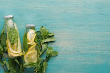 mavi ahşap yüzeyde limon ve salatalık dilimleri ve nane ile şişeler içinde Detox içmek üst görünümü