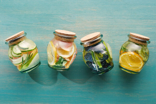 top view of detox drinks in jars with citrus fruits on blue wooden surface