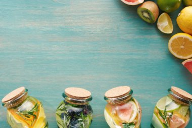 ahşap mavi yüzeyde meyve, sebze, otlar, meyveler ve yeşilliklerle yakın kavanozlarda detoks içeceklerin üst görünümü