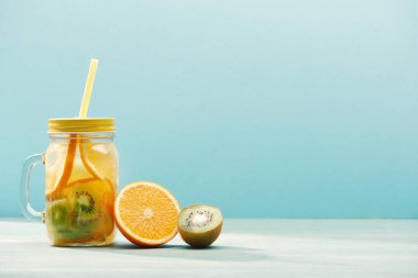 mavi üzerinde izole turuncu ve kivi yakın saman ile kavanoz içinde Detox içecek