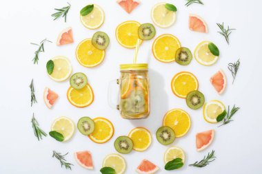 flat lay with sliced kiwi, oranges, lemons, grapefruits, mint, rosemary and detox drink in jar with straw on grey background clipart