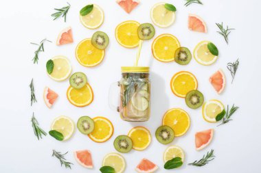 flat lay with sliced kiwi, oranges, lemons, grapefruits, mint, rosemary and detox drink in jar on grey background clipart