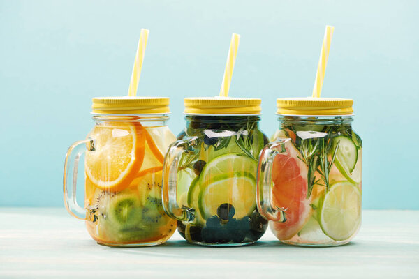 fresh organic detox drinks with berries, fruits and vegetables in jars with straws isolated on blue 