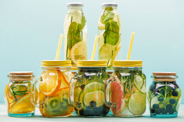 organic detox drinks with berries, fruits and vegetables in jars and bottles with straws isolated on blue 