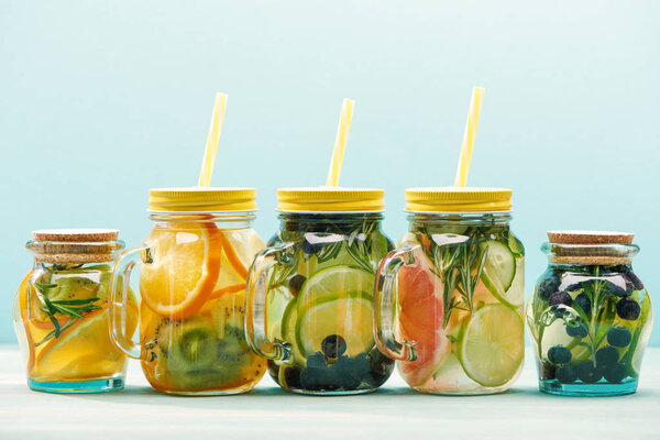 fresh detox drinks with berries, fruits and vegetables in jars with straws isolated on blue 