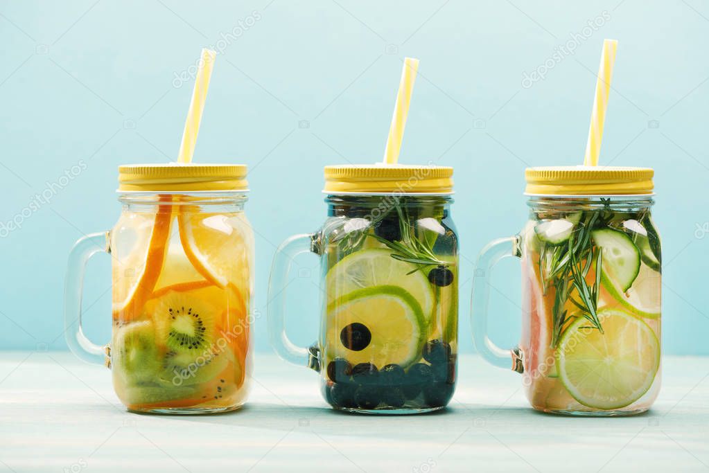 organic detox drinks with berries, fruits and herbs in jars with straws isolated on blue 