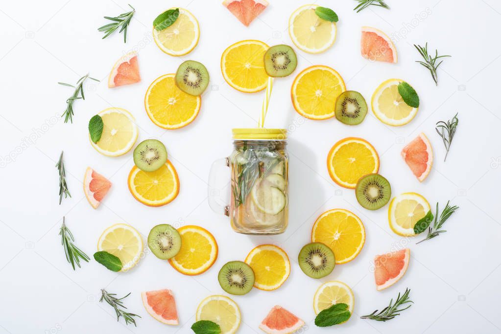 flat lay with sliced kiwi, oranges, lemons, grapefruits, mint, rosemary and detox drink in jar on grey background