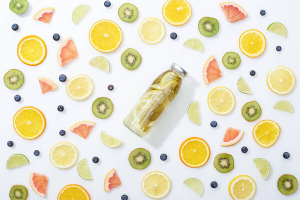 top view of detox drink in bottle among fruits and blueberries on white background