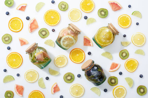 top view of detox drinks in jars among fruits and blueberries on white background