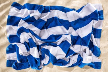 kum üzerinde buruşuk mavi ve beyaz çizgili plaj havlusu üst görünümü