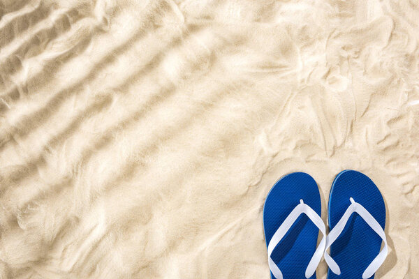 top view of white blue flip flops on sand with shadows and copy space
