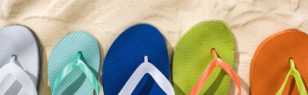 panoramic shot of white, turquoise, green and blue flip flops on sand