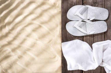 Top view of white flip flops and towel on wooden brown board and sand with copy space clipart