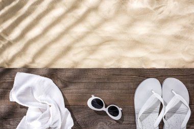 top view of sand with copy space and white towel, retro sunglasses and flip flops on wooden brown board  clipart