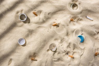 top view of seashells, bottle caps, scattered cigarette butts, plastic bottle caps on sand clipart
