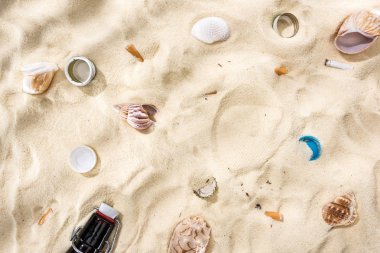 top view of seashells, bottle caps, scattered cigarette butts and glass bottle on sand clipart