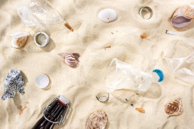 top view of seashells, bottle caps, scattered cigarette butts, plastic cups, glass bottle and candy wrapper on sand clipart