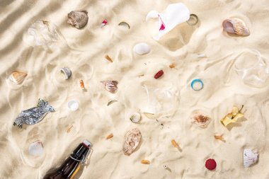 top view of seashells, scattered cigarette butts, apple core, plastic cups, glass bottle and candy wrapper on sand clipart