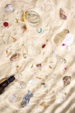 kum kabukları, cam şişe, dağınık sigara izmaritleri, kırık camlar, elma çekirdeği, plastik bardak ve kum üzerinde şeker sarma üst görünümü