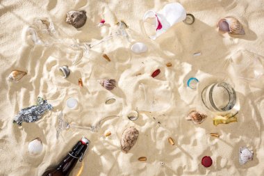 kum kabukları, cam şişe, dağınık sigara izmaritleri, kırık camlar, elma çekirdeği, plastik bardak ve kum üzerinde şeker sarma üst görünümü