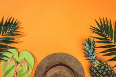 ananas üst görünümü, tropikal yaprakları, yeşil parmak arası terlik ve kopya alanı ile turuncu arka plan kahverengi hasır şapka
