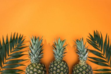 kopya alanı ile turuncu arka plan üzerinde ananas ve tropikal yaprakların üst görünümü