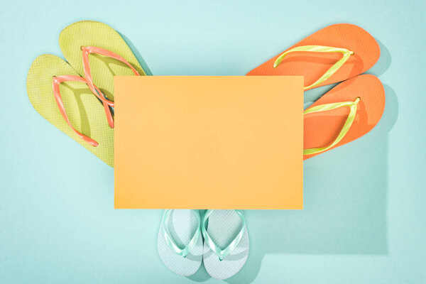 top view of green, orange and turquoise flip flops and empty card with on background