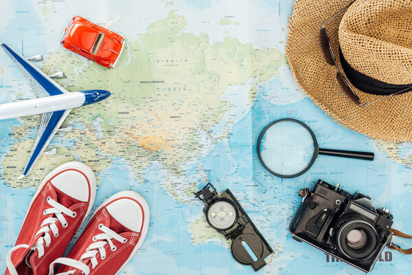 Top view of gumshoes, straw hat, magnifier, toy plane, toy car, sunglasses, film camera and compass on world map