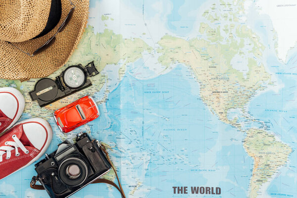 Top view of gumshoes, straw hat, sunglasses, film camera, toy car and compass on world map