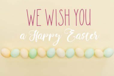 top view of painted pastel chicken eggs on light yellow background with we wish you a happy Easter lettering clipart