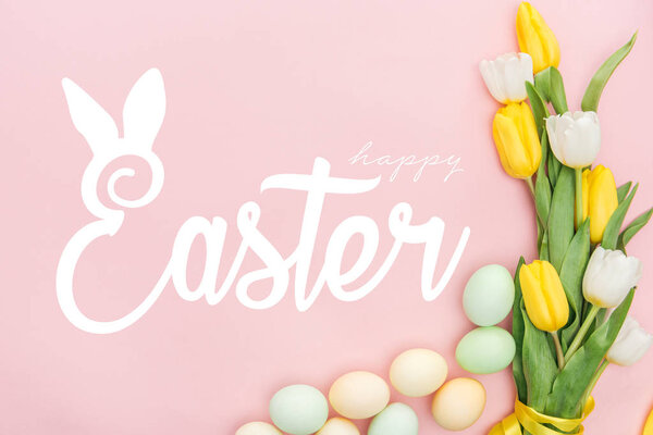 top view of painted chicken eggs and bright tulips on pink background with happy Easter lettering