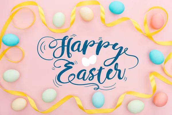 画五彩鸡蛋和缎黄色丝带在粉红色背景与快乐复活节字母的顶视图 — 图库照片