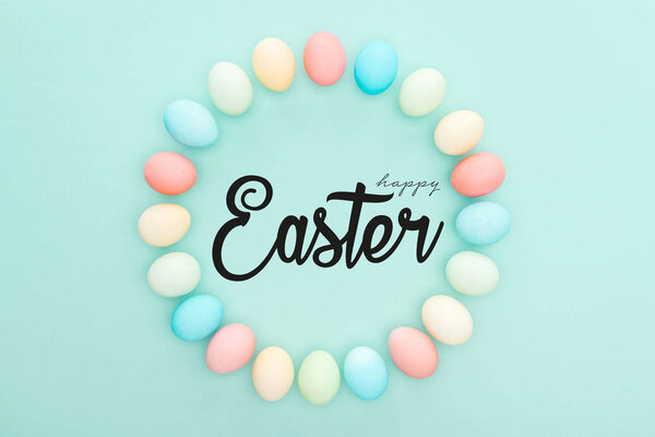 top view of round frame made of painted chicken eggs on blue background with black happy Easter lettering