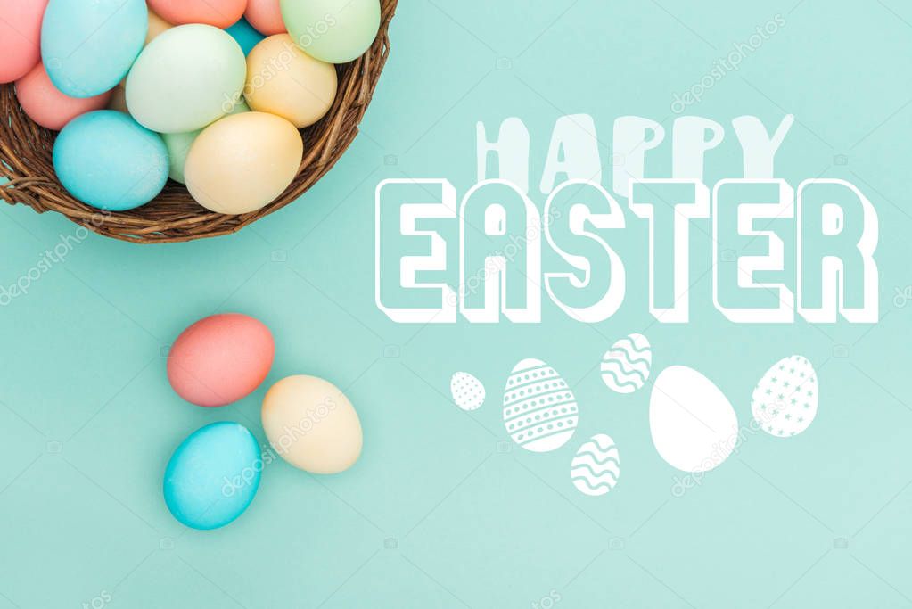 top view of multicolored painted eggs in wicker basket with happy Easter lettering on blue background
