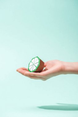 cropped view of young woman holding handmade paper lime on turquoise with copy space clipart