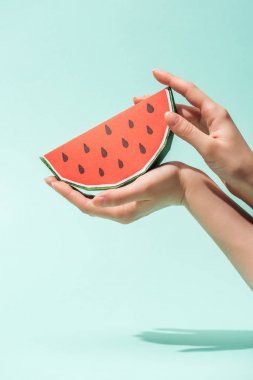 cropped view of young woman holding paper watermelon with seeds on turquoise clipart