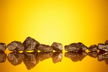 gold shiny stones in row with reflection on yellow background with copy space clipart