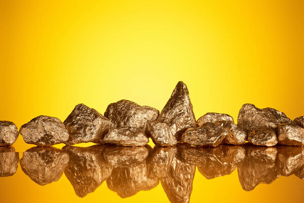 pile of gold shiny stones in row with reflection on yellow background with copy space