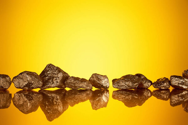 gold shiny stones in row with reflection on yellow background with copy space