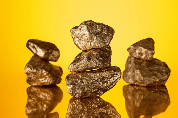 selective focus of three stacks of gold shiny stones with reflection isolated on yellow 