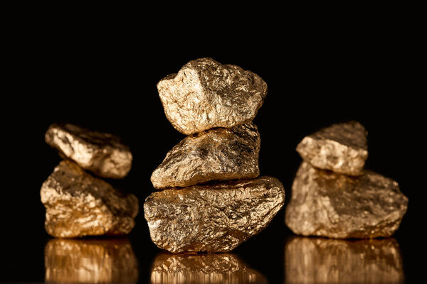 selective focus of three stacks of gold shiny stones with reflection isolated on black