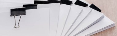 panoramic shot of stacks of blank paper with metal binder clips on table clipart